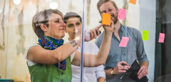 3 creatives looking at stickie notes on glass window.